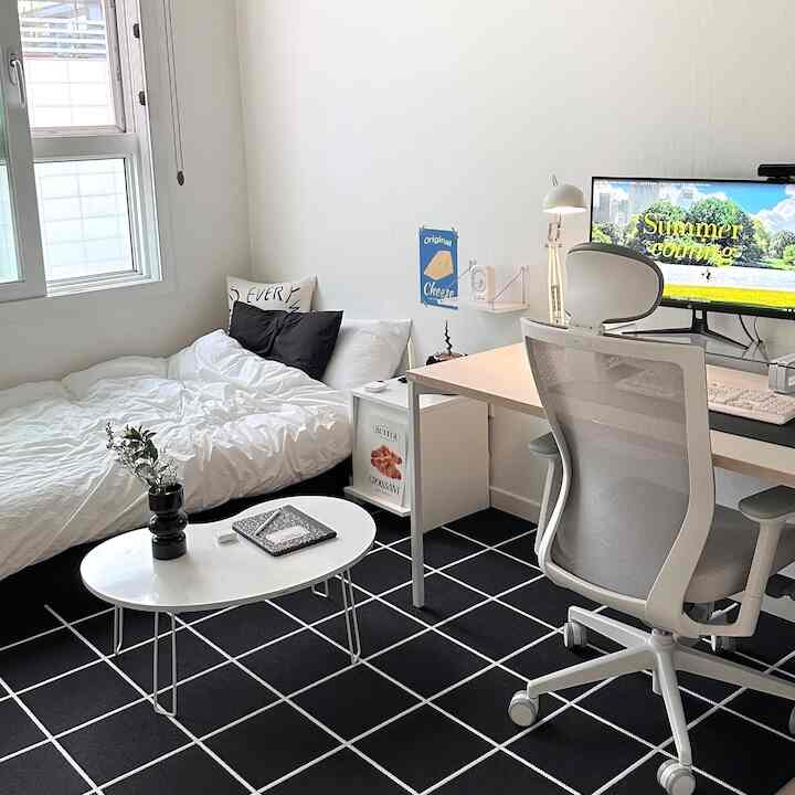 白と黒のモノトーンの一人暮らし寝室兼ホームオフィス空間、大きな格子柄ラグとデスク・オフィスチェアが配置されたシンプルモダンなインテリア