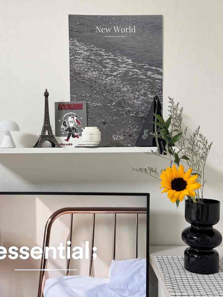 白い壁の寝室に黒い花瓶とヒマワリの花、ウォールデコが配置された雰囲気のあるインテリア