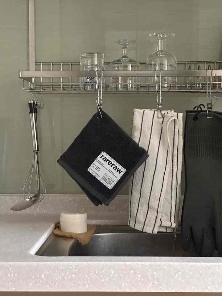 ホワイトとグレーのトーンの清潔なキッチンシンクとステンレスの棚にタオルやゴム手袋が掛けられた、実用的でモダンな雰囲気のあるインテリア