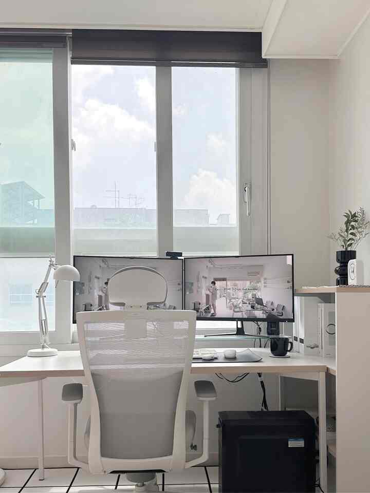 ホワイトとブラックのトーンのホームオフィス、窓辺に置かれたデスクとチェア、デュアルモニターが整った作業環境を演出