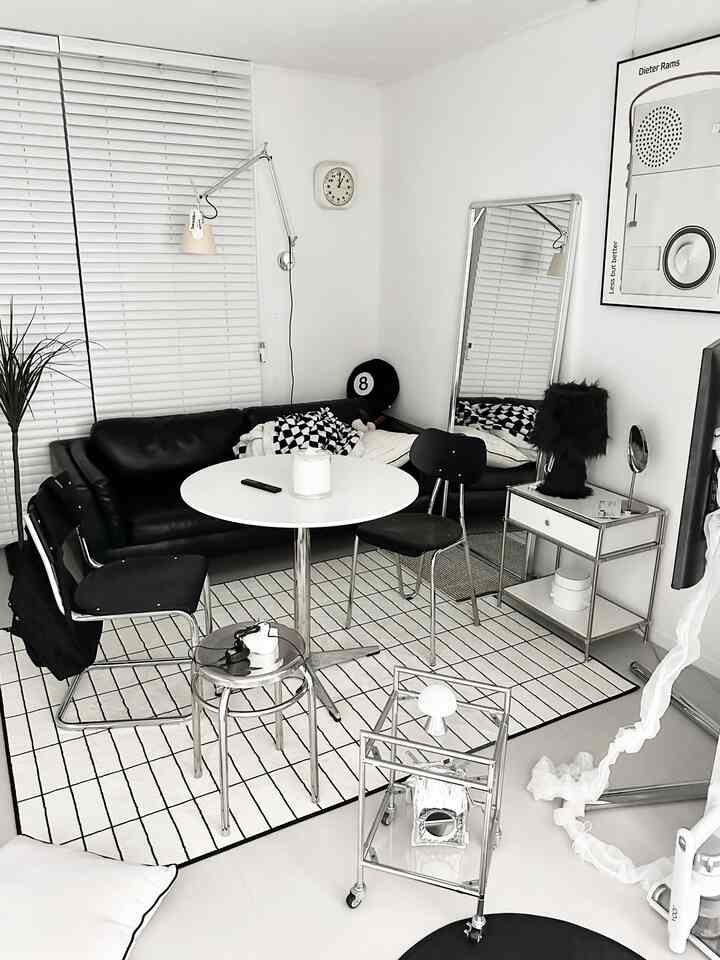 白と黒のモダンなリビングルーム、黒のレザーソファ、丸テーブル、金属スツール、全身鏡が配置されたシンプルなインテリア