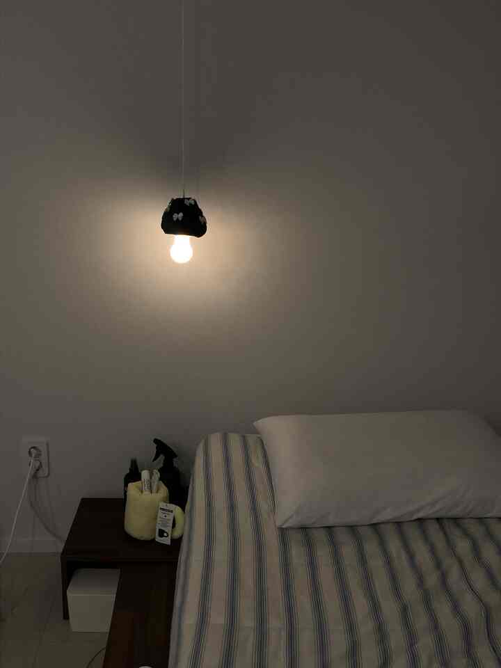 白い壁とブラウンのナイトテーブル、ストリングライトがあるシンプルな寝室、ストライプの寝具のベッド