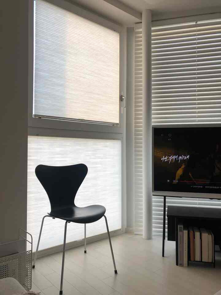 白と黒の調和が取れたリビング、カスタムブラインドとモダンチェア、サムスンのセリフテレビが配置されたすっきりとした空間