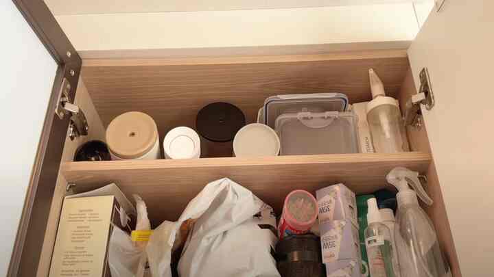 明るい木目調の棚にさまざまな密閉容器とスプレーボトルが整頓された狭いワンルームの玄関の靴箱収納スペース
