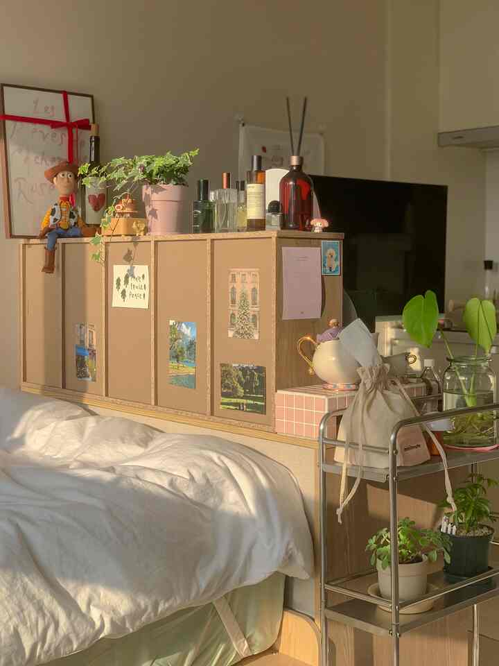 ホワイトとウッドトーンが調和した6畳の寝室、棚の上に香水や鉢植え、キャラクターフィギュアが配置された温かみのあるナチュラル空間