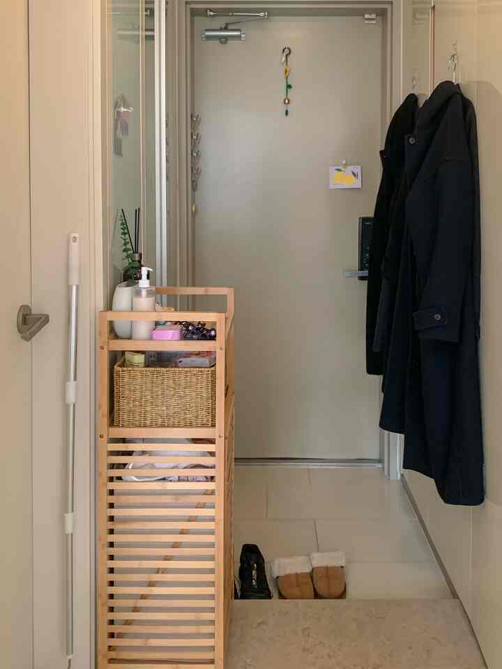 ベージュ色調の玄関、木製収納ラックとラタンバスケットが配置されたナチュラルな雰囲気の空間