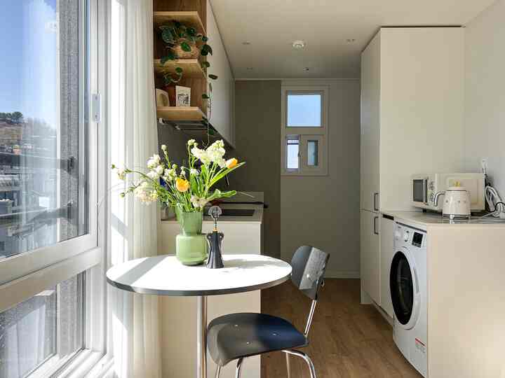 明るい白と木目調の色合いの小さなキッチン、丸テーブルと一脚の椅子が置かれた落ち着いた空間