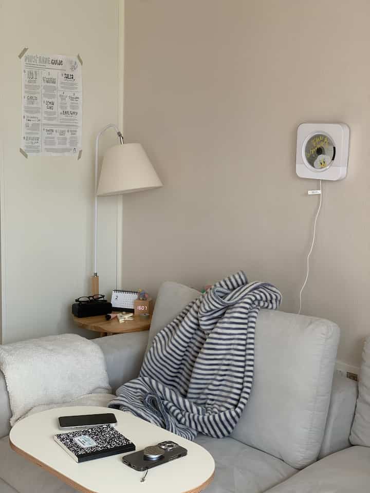 白とベージュの色調のリビング、グレーのソファにストライプのブランケットが掛けられた雰囲気のある空間