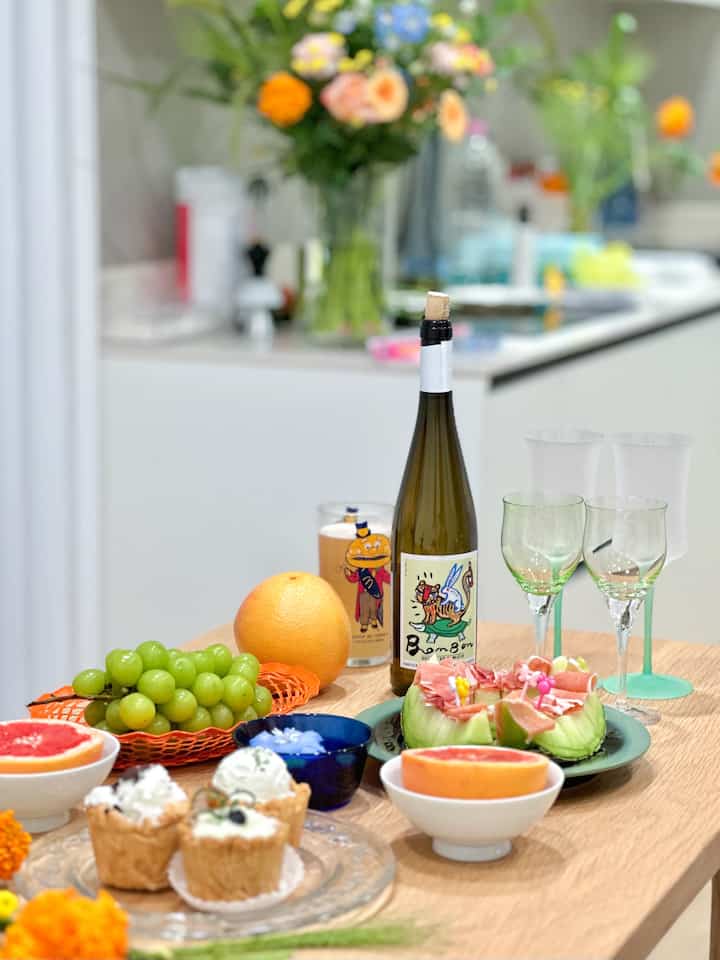 ナチュラルな木目調のダイニングテーブルに果物やケーキ、ワインボトルとグラスが並ぶ雰囲気のあるキッチンのホームパーティー空間