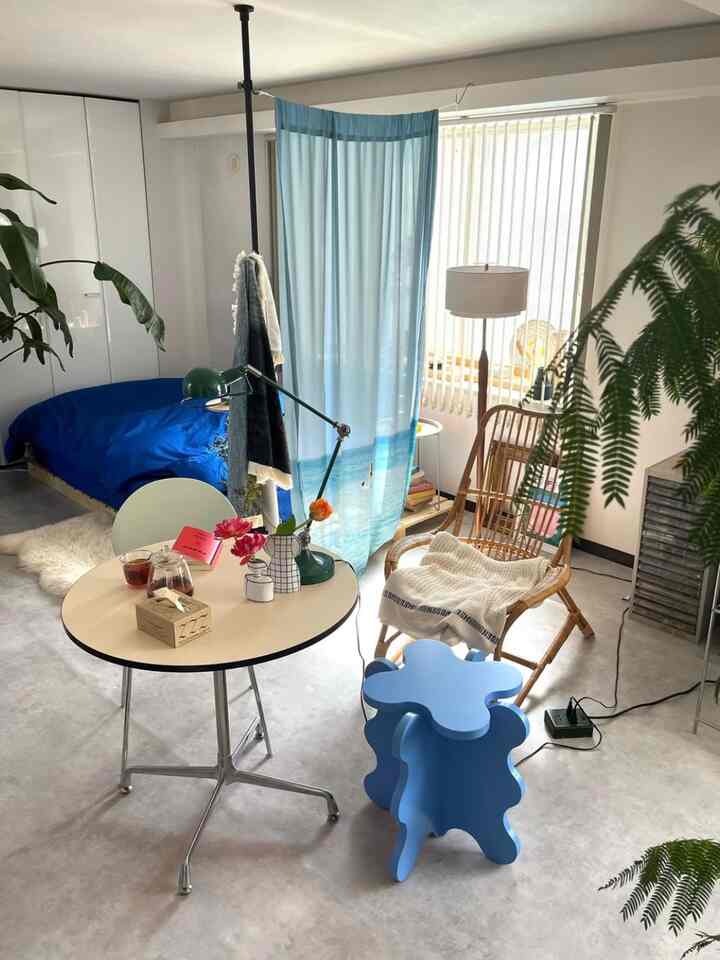ナチュラルな色調とブルーを基調としたワンルーム寝室、ナチュラルウッドの椅子とカーテン、デスクが配置された印象的な空間
