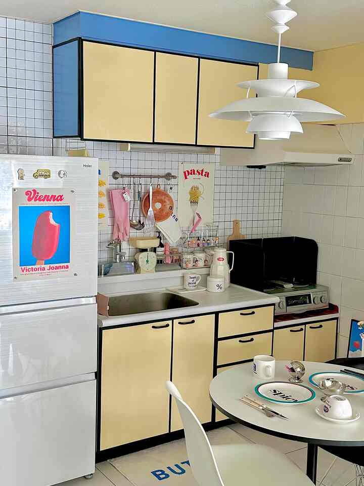 黄色と白を基調としたキッチン、リメイクされたキャビネットとタイルシートの壁が配置された印象的な空間