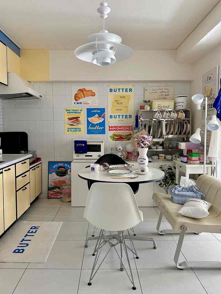 ホワイトとイエローの色調のダイニングルーム、丸テーブルと椅子、ステンレス製の収納ラック、壁のポスターが配置された雰囲気のあるインテリア