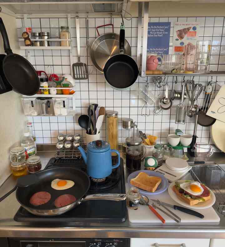 白いタイル壁とステンレス調理台のモダンなキッチン、フライパンとコーヒー器具が配置された印象的な空間