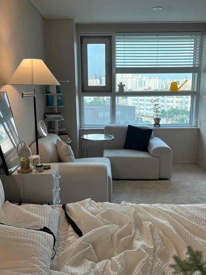 明るいホワイトトーンの寝室兼リビング、モジュラーソファと大きな窓が配置された印象的な空間