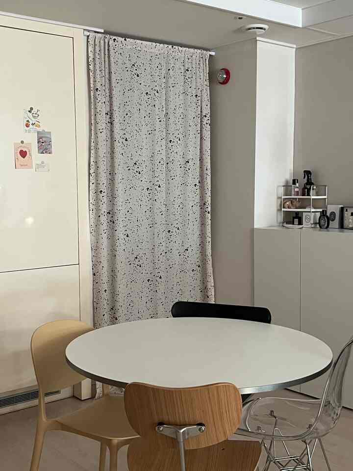 白とベージュのトーンのダイニングルーム、丸いテーブルと様々な椅子、柄のカーテンが配置されたモダンな空間