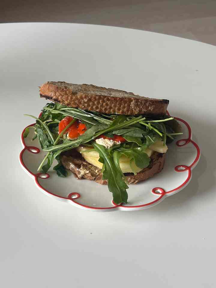 赤い縁取りの白いレトロ皿に、全粒粉パンと新鮮な野菜が挟まれたサンドイッチ