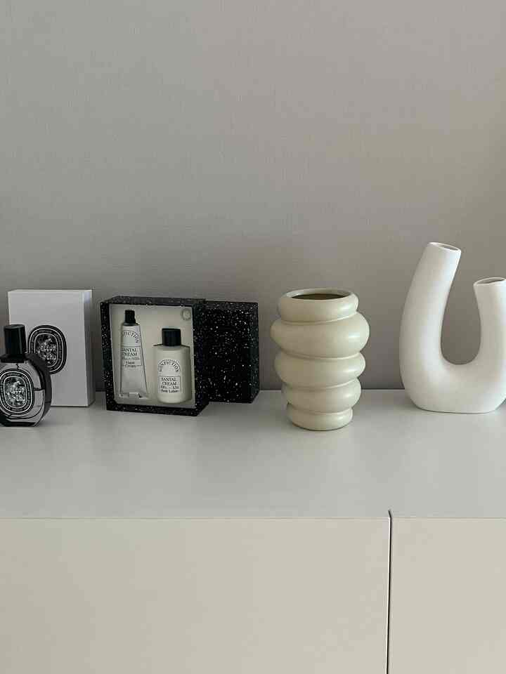 白とナチュラルカラーのキッチンキャビネットの上に香水と陶器のオブジェが並べられた、落ち着いたミニマルな空間