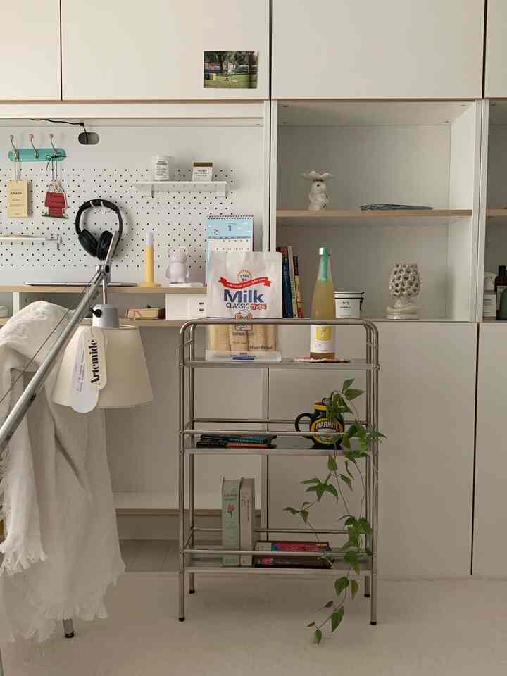 明るいホワイトとシルバーの壁面収納と棚、ステンレス製のワゴンと植物が配置されたミニマルな空間