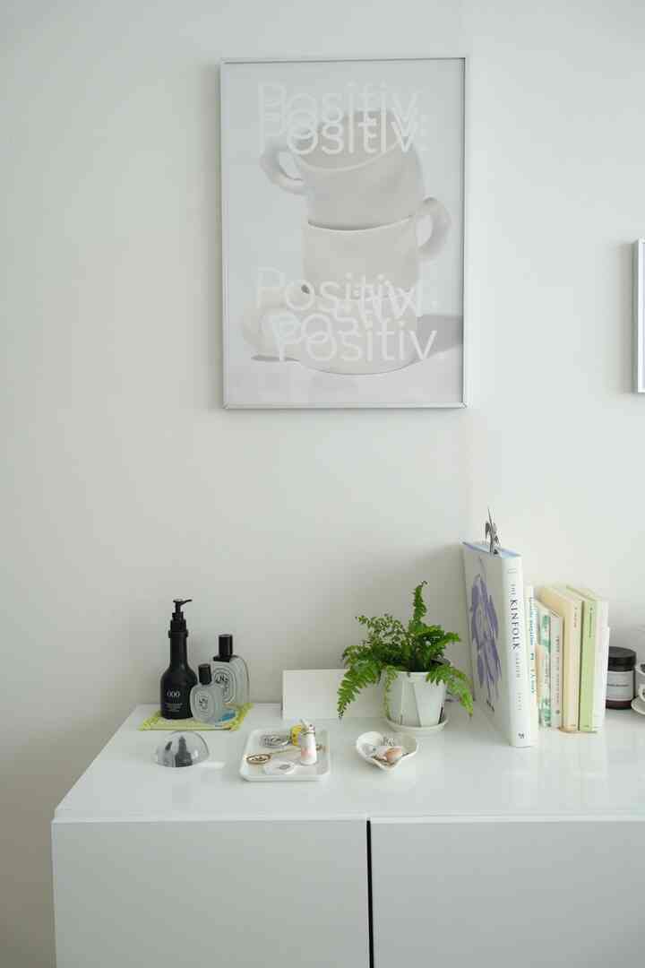 白を基調とした壁に白いカップのポスターが掛かり、白いキャビネットの上には植物と本、小物が配されたミニマルな空間