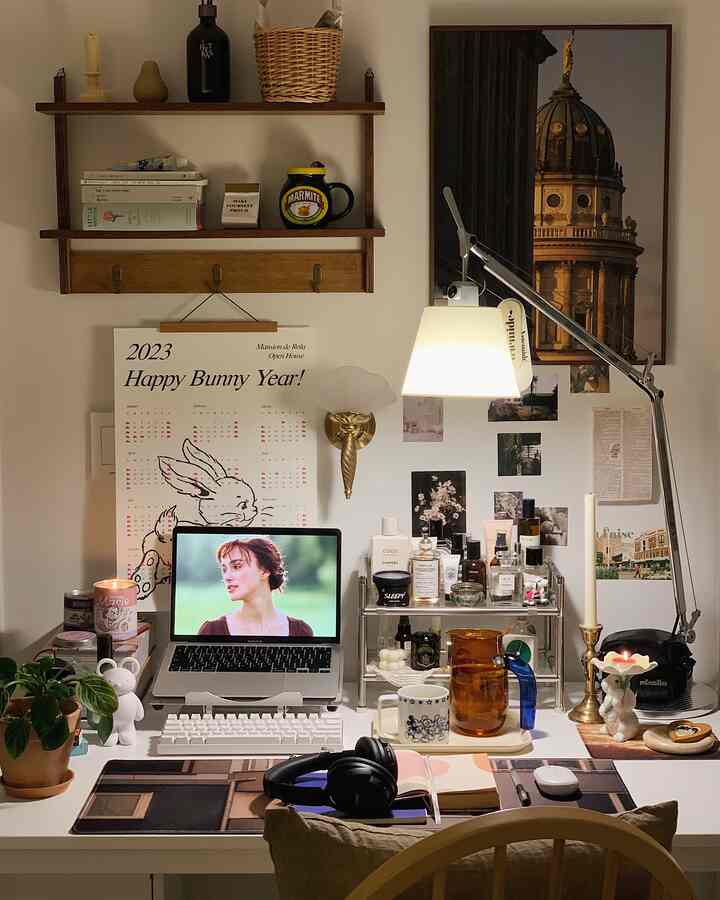 ナチュラルカラーと白い壁のホームオフィス空間、中央のデスクにノートパソコンと照明、壁には棚とカレンダーが配された雰囲気のあるインテリア