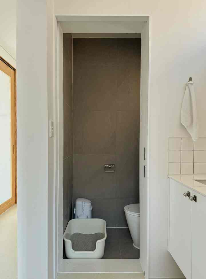 グレーのタイル壁と床に猫トイレが置かれた、ミニマルでコンパクトなトイレ空間