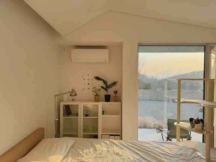 ナチュラルな色調と白を基調とした広々とした寝室、ベッドとドレッサー、キャットタワーの上でくつろぐ猫がいる印象的なインテリア