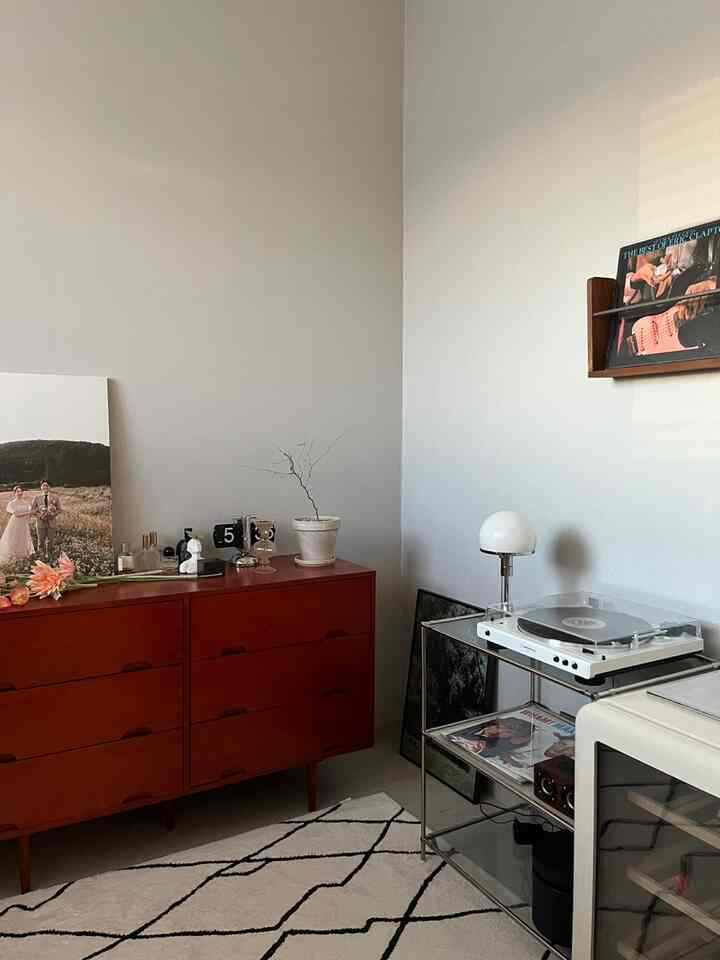 白い壁とヴィンテージ風の赤いチェストが配置されたリビング、ターンテーブルとモジュール棚でアナログ音楽鑑賞の雰囲気あるインテリア