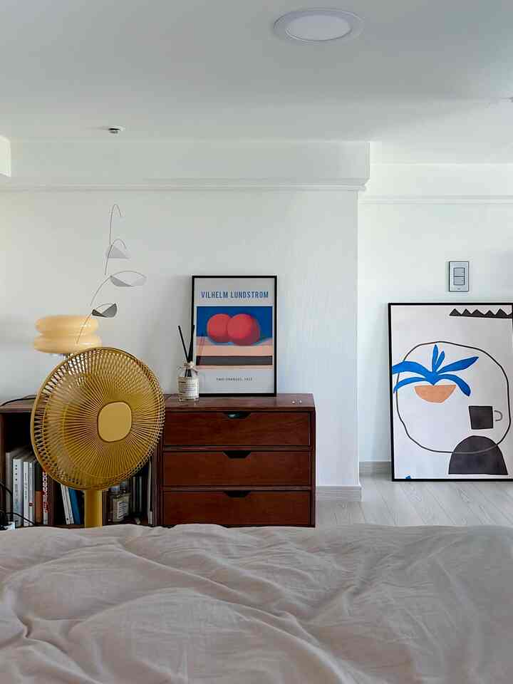 白とナチュラルブラウンの寝室、モダンな額縁とモビールが配置された雰囲気のある空間