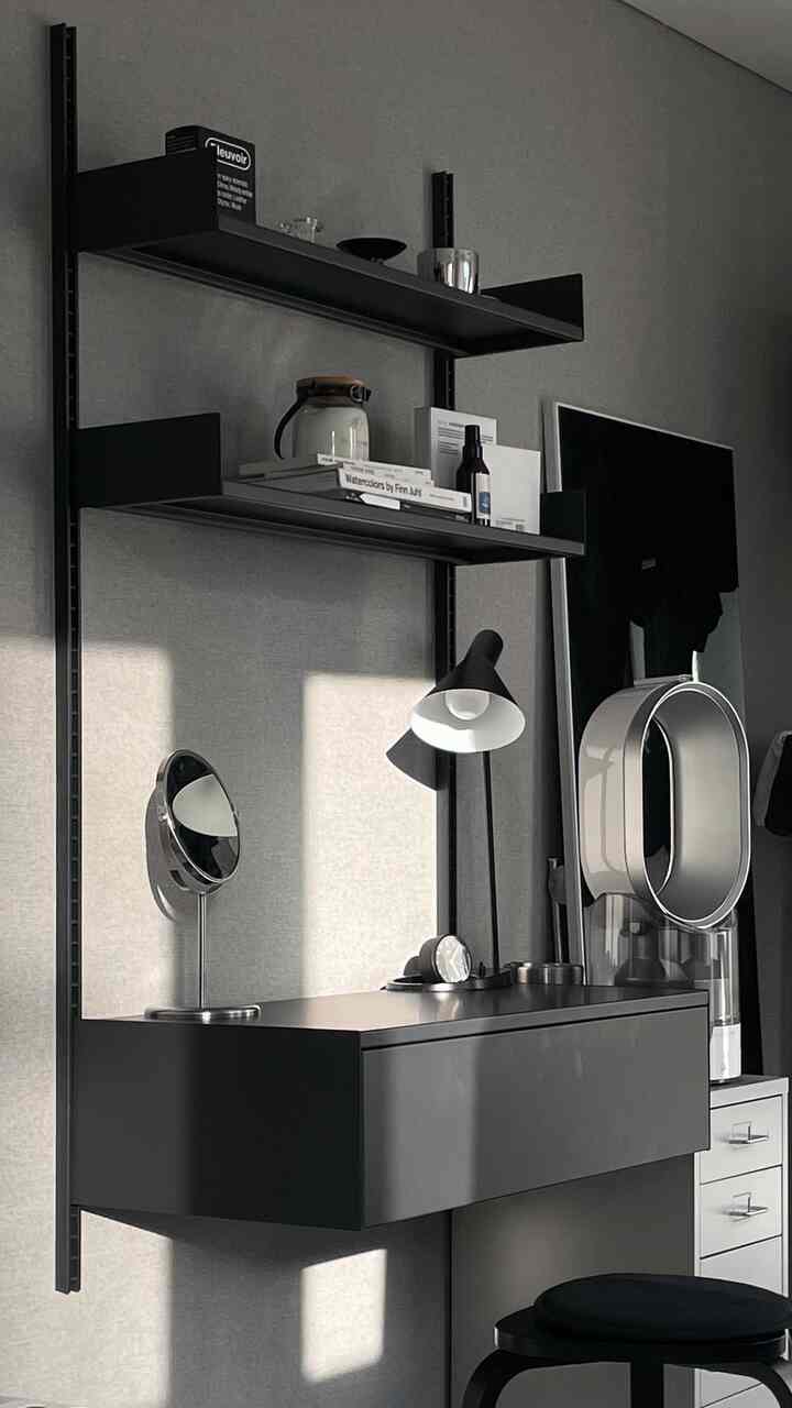 グレーの壁を背景にブラックの化粧台と壁掛け棚が配置されたコンパクトな寝室の雰囲気のあるインテリア