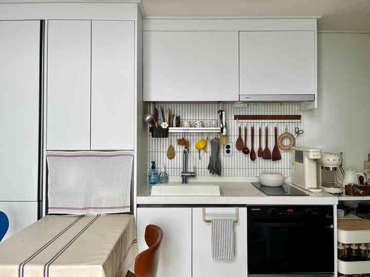 白を基調としたキッチン、木製の調理器具とテーブルクロスが配置された清潔感のある空間