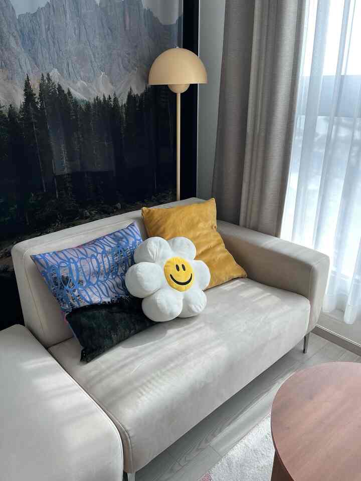 ベージュのソファと黄色いクッションが配置されたリビング、自然の風景柄のファブリックポスターとマッシュルーム型のフロアランプが印象的なミッドセンチュリーモダンのインテリア