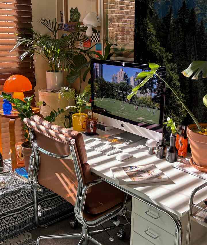 温かみのある木目調とホワイトが調和したホームオフィスで、ミッドセンチュリーモダンのデスクとチェア、多数の植物が配置された居心地の良い作業空間