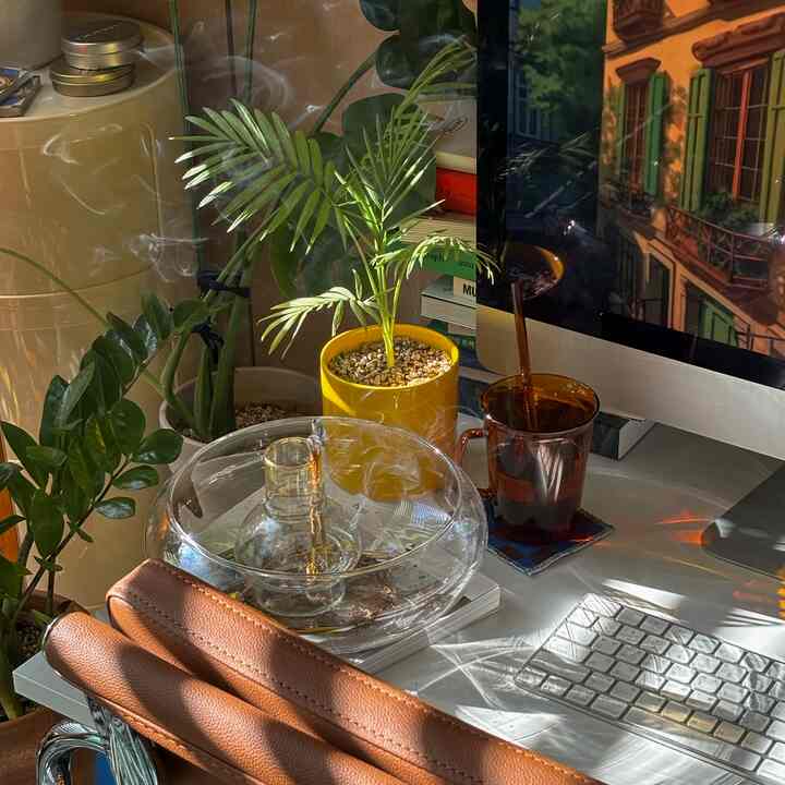 白いデスクとブラウンのレザー椅子、多数の植物とインセンスの煙が調和した雰囲気のあるホームオフィス