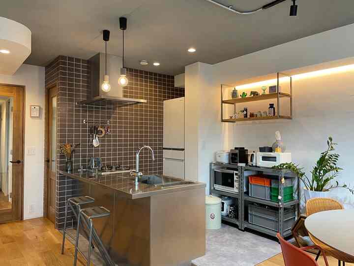 ステンレスと木目調が調和したインダストリアルスタイルのキッチンとダイニング、ゴールドアクセントとペンダントライトが印象的な空間