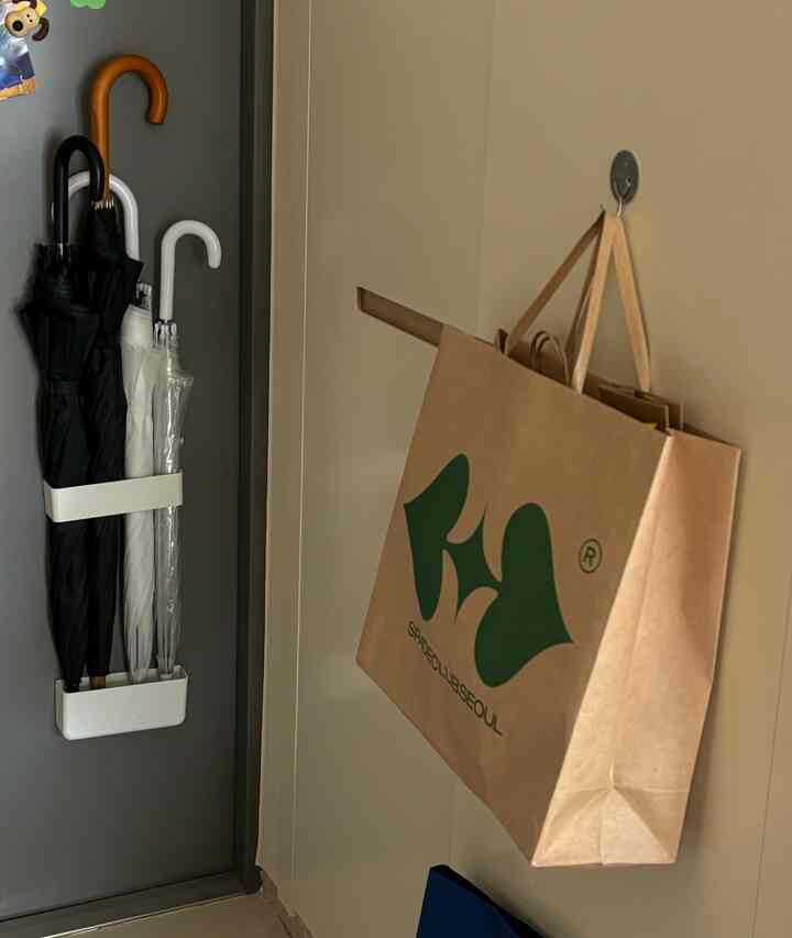 ベージュ調の玄関、壁にショッピングバッグと傘が整頓された収納アイデアが光る印象的な空間