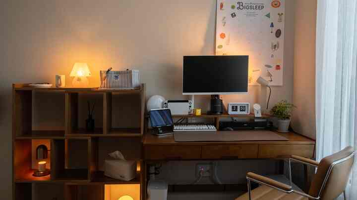 ベージュの壁と木目調のデスク、書棚が配置されたホームオフィス空間、ニンテンドースイッチ、時計、植物がある雰囲気のある作業空間