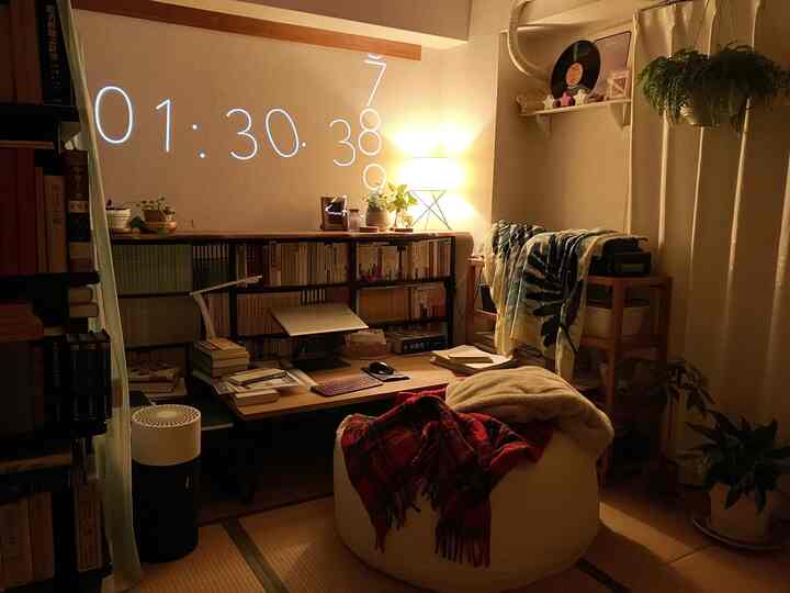 暖かい照明のナチュラルトーンのリビングスペース、本棚とローテーブル、ビーズクッションが配置された雰囲気のある書斎のような部屋