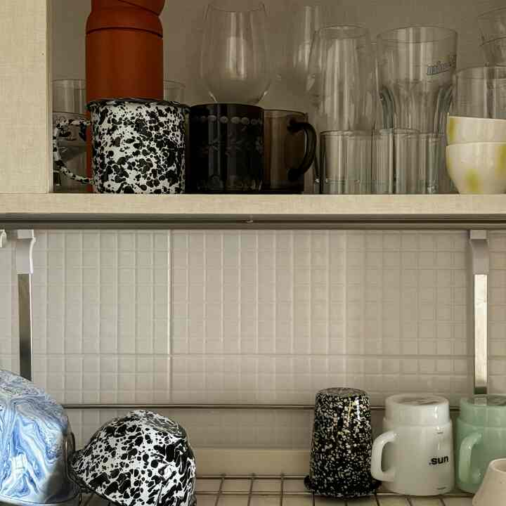 白いタイル壁と大理石柄のマグカップが置かれた、1人暮らしのためのホームカフェのあるキッチン棚