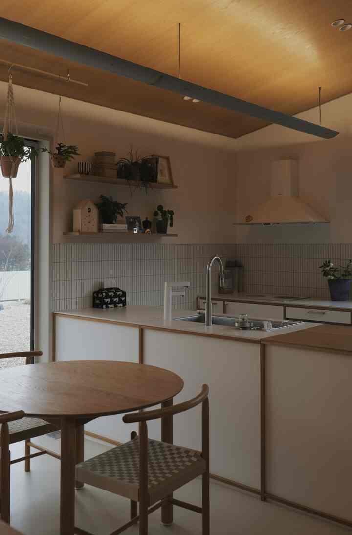 木目調の天井とナチュラルなキッチン、丸いダイニングテーブルが配置されたシンプルな空間