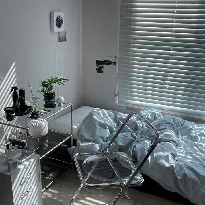 グレーのブラインドと透明な椅子が配置された一人暮らしの寝室、落ち着いた雰囲気の空間