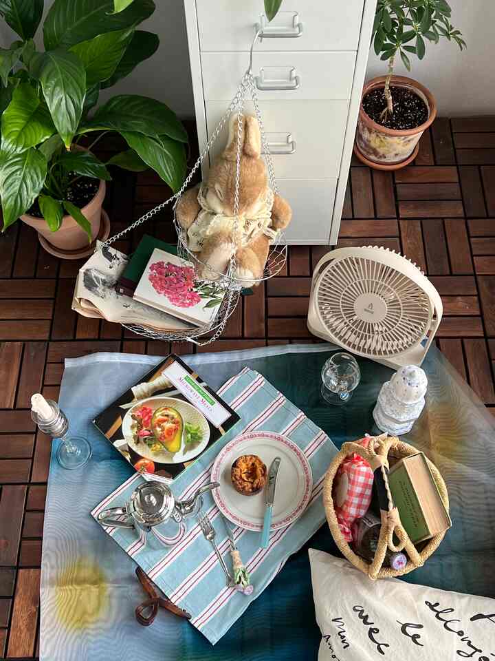 木目調の床と白いキャビネットがあるベランダ、ピクニックマットと小物が配置された雰囲気のある空間