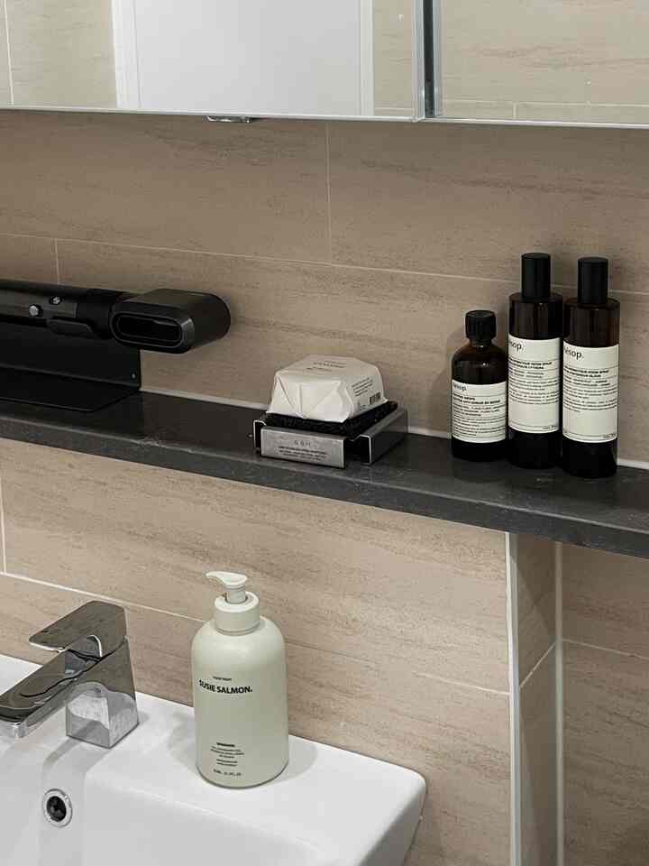 ベージュとグレーの色調のバスルーム、洗面台と棚にハンドウォッシュとアロマスプレーがきれいに配置された印象的な空間