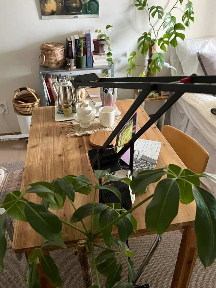ナチュラルな木目調と緑の植物が調和するホームオフィス兼読書スペース、シンプルで居心地の良いデスクとテーブルランプ配置
