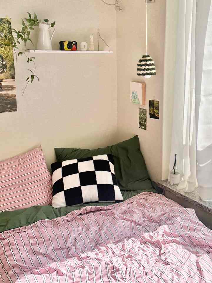 白とナチュラルカラーの寝室、ピンクとグリーンの寝具が配置された暖かくシンプルな雰囲気のインテリア