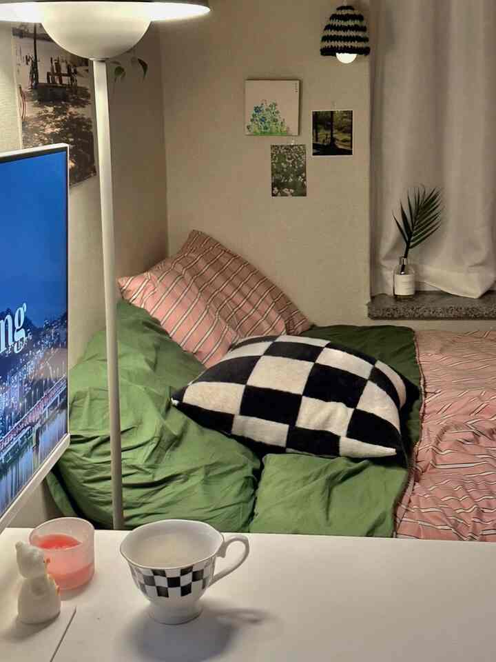 白い壁と緑の寝具が調和した寝室、フロアランプと編みのムードライトが居心地の良い雰囲気を演出するインテリア