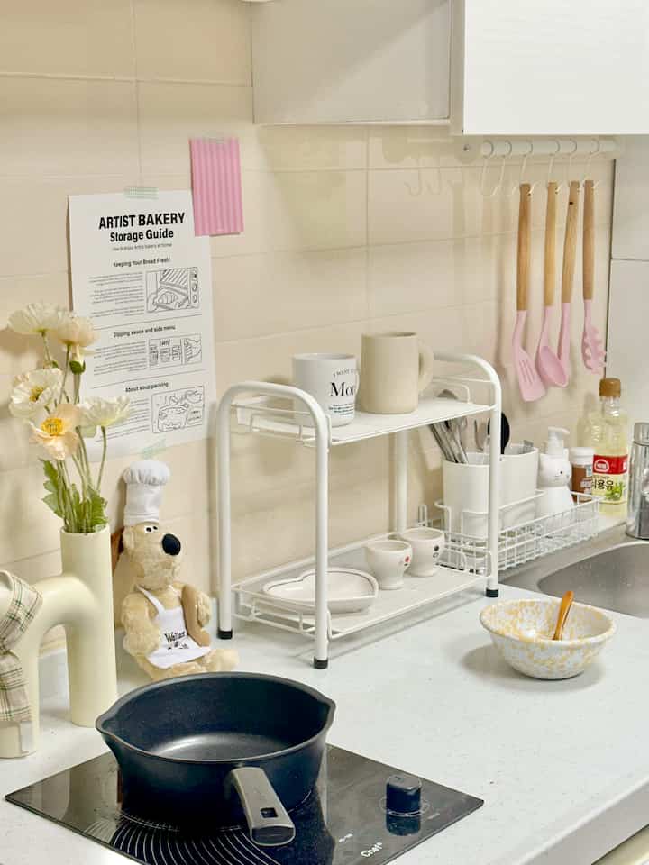 白とナチュラルな色調のキッチン、調理器具や収納ラック、コック帽をかぶったグロミット人形と花瓶が配置された雰囲気のある空間