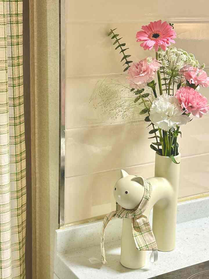 ベージュ色調の壁に、アイボリー色の猫型花瓶とチェック柄のカーテンが配置されたキッチンの印象的な空間