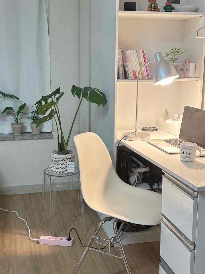 ホワイトとウッドトーンの調和が取れた一人暮らしの作業スペース、デスクとプラスチックチェア、デスクライトが落ち着いた雰囲気を演出