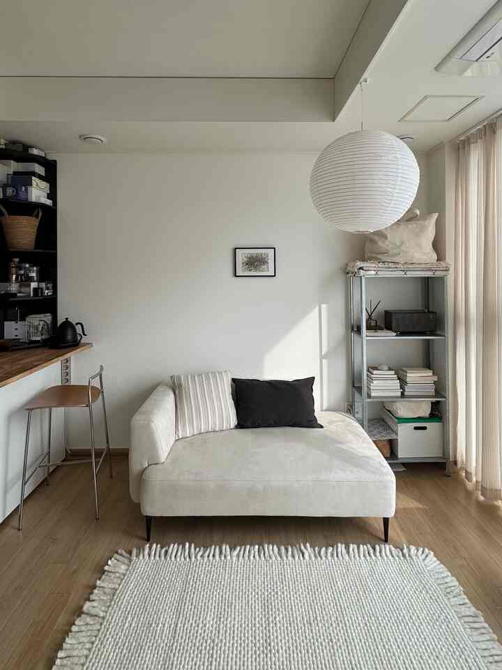 白い壁と木目調の床が調和する一人暮らし向けのリビング、ベージュのソファとラグが配置されたミニマルでナチュラルなインテリア