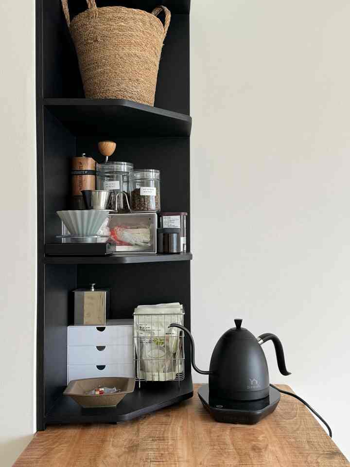 黒のコーナー棚と木目調のテーブルに配置されたドリップコーヒーセットがあるシンプルでモダンなおうちカフェ空間